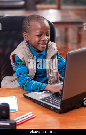 Young African boy sitting at his father's desk, playing on the laptop Stock Photo