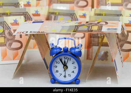 Miniature clock showing five to twelve with banknotes in the background Stock Photo