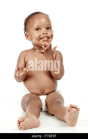 An infant sits in front of a white background with chocolate all over her face Stock Photo