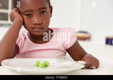 Young African child sitting at the dinner table, unhappy with the prospect of eating peas Stock Photo