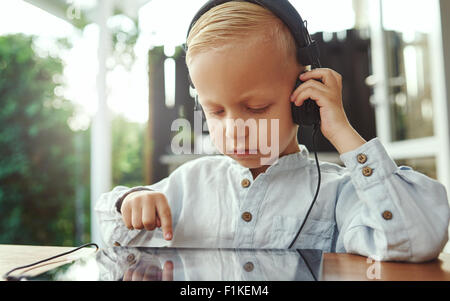 Little boy listening to his selected music soundtrack that he has chosen off the touch screen on his tablet computer with his ey Stock Photo