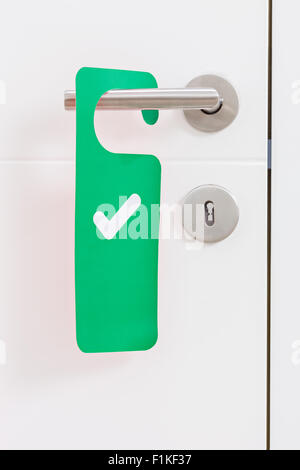 Close-up on a metal handle of a white door with a green access plate with check mark on it Stock Photo