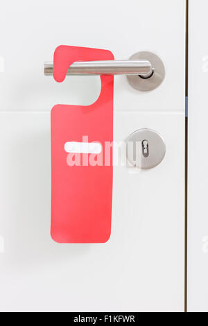 Close-up on a metal handle of a white door with a red do not disturb label on it Stock Photo