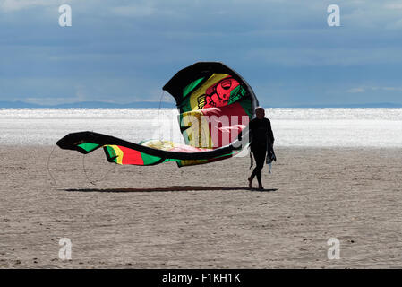 A solitary kitesurfer  walks with his equipment along the sandy beach at St Annes in Lancashire Stock Photo
