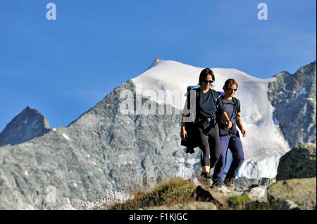 Two female hikers walking along mountain path in the Pennine Alps, Valais / Wallis, Switzerland Stock Photo