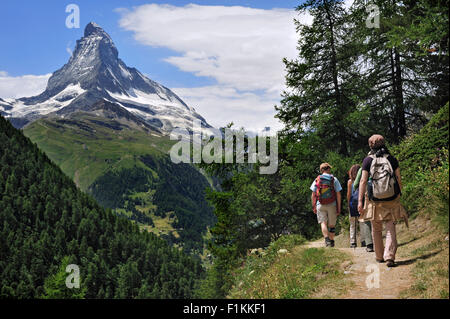 Hikers walking through larch forest with view over the Matterhorn mountain in the Swiss Alps, Valais / Wallis, Switzerland Stock Photo