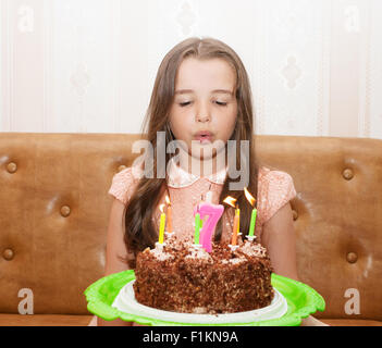 little girl 7 years old blowing out the candles on a birthday cake Stock Photo