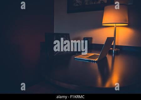 Night Work Desk. Dark Serene Theme with Laptop and Night Lighting.  Wooden Desktop. Stock Photo