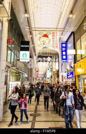 Dotonbori area of Osaka. View along side street now covered shopping arcade in the evening. Illuminated and busy with people walking. Stock Photo