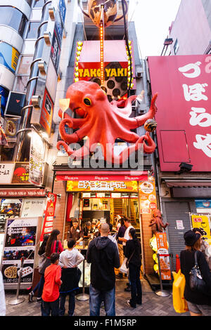 Japan, Osaka. Dotonbori. People outside Takoyaki restaurant, Dotonbori Kukuru Honten, with large red octopus sign above take away window. Stock Photo