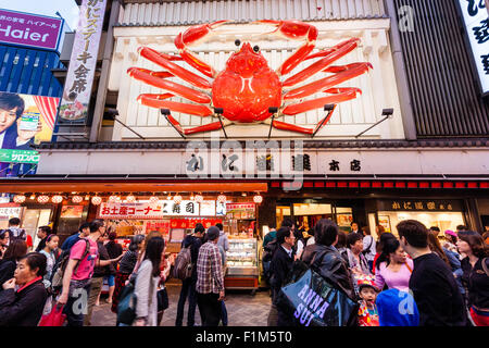 Osaka, Dotonbori. Exterior of famous crab restaurant, Kani Doraku, with giant mechanical orange crab above entrance. Street busy with people walking. Stock Photo