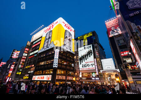 Osaka. Dotonbori, Ebisubashi bridge. Night. Famous massive Asahi beer sign and others on adjacent buildings, with crowds of people viewing on bridge. Stock Photo