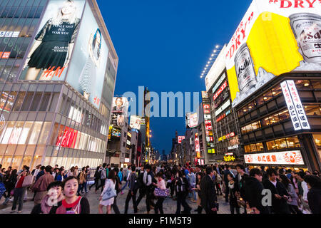 Japan, Osaka. Crowds of people at night, walking across Ebisubashi bridge at Dotonbori between the H&M store and Asashi famours illuminated beer sign. Stock Photo