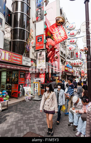 Japan, Osaka. Dotonbori. People outside Takoyaki restaurant, Dotonbori Kukuru Honten, with large red octopus sign above take away window. Stock Photo