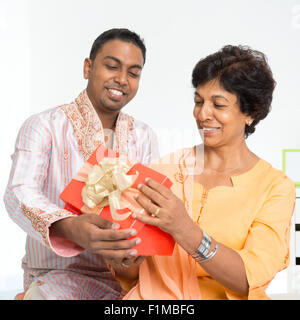 Portrait of happy Indian family celebrate birthday at home. Mature 50s Indian mother received surprised present from her 30s gro Stock Photo