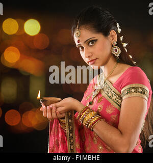 Indian girl in traditional sari lighting oil lamp and celebrating Diwali or deepavali, fesitval of lights at temple. Female hand Stock Photo