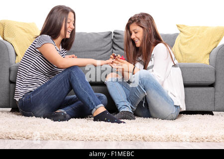 Two teenage girls sitting on the floor in front of a gray sofa and polishing their nails isolated on white background Stock Photo