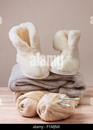 Pair of warm winter sheepskin slippers (alpaca), wool yarn , pile of warm woolen clothes (Selective focus) Stock Photo