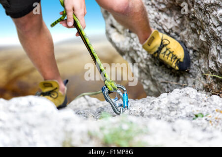 Climber reaches the summit of a mountain. Focus is on the rope and the carabiner Stock Photo