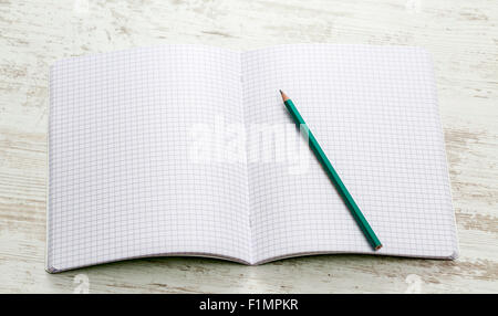 Upper view of an open notebook with squares with and a graphite pencil on a white wooden table. Stock Photo