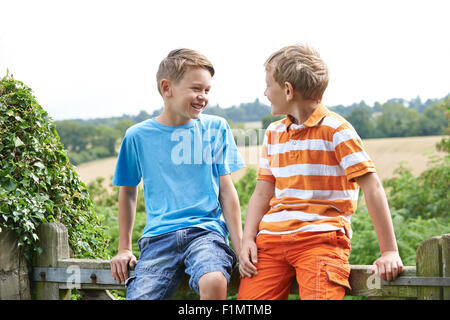 Two Boys Sitting On Gate Chatting Together Stock Photo