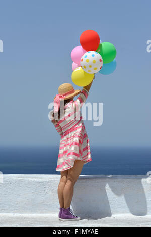 Young woman in dress holding colorful balloons at Santorini Stock Photo