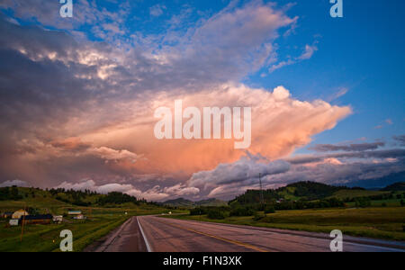 Looking down a empty highway with a pretty sunset on the distant horizon with dark, ominous clouds in the sky Stock Photo