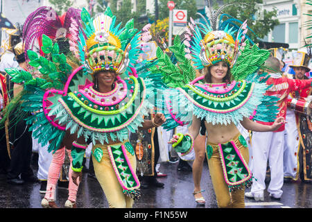 Two female participants dressed in exotic green clothes, dancing, as the parade passes through Notting Hill Stock Photo