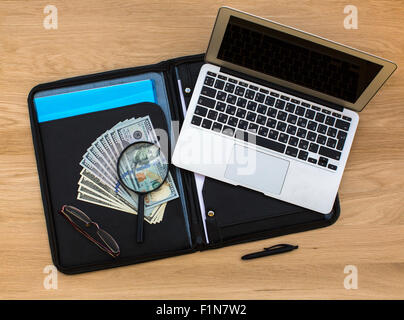 US hundred dollar bills under magnifying glass on business folder and Laptop lying on oak wood texture, top view. Stock Photo