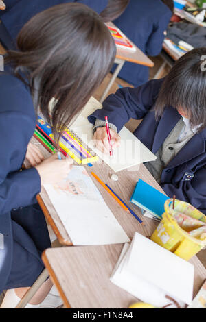Japanese schoolgirls drawing with color pencils on wooden table Stock Photo