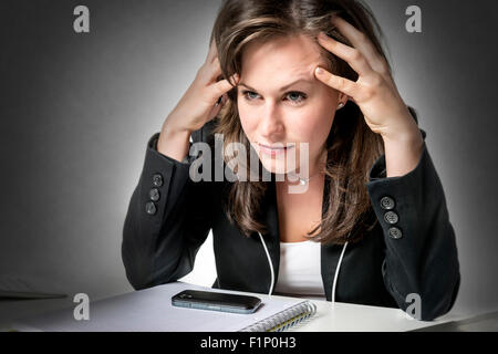 Stressed business woman sitting in office at desk, looking at laptop and holding his hands to his head