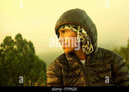 Young handsome man with beard in autumn dark jacket hooded down in the wild looks away. Filter was used. Stock Photo