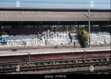 Amritsar, Punjab, India. Rice bags stacked on a platform at the station waiting to be loaded onto trains with workers ready and a truck delivering more. Stock Photo