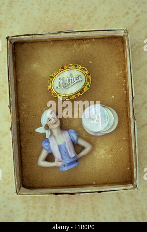 Small cardboard box containing porcelain half-doll from pin-cushion mother-of-pearl buttons and brooch stating Mother Stock Photo