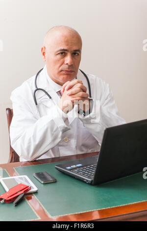Doctor in his studio at desk, on pc,  with glasses. Use new technologies. In his professional studio, he is sitting at antique d Stock Photo