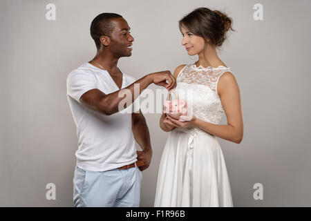 Three Quarter Shot of a Young Couple with Piggy Bank Smiling at each other Against Gray Wall. Stock Photo