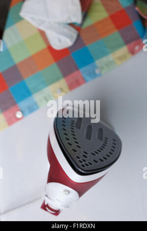 Top view of iron on ironing board near the plaid shirt. Focus on iron's tip Stock Photo