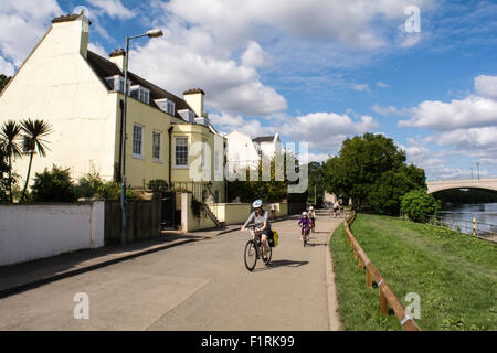 A young family cycling along the Thames on a sunny morning at Mortlake