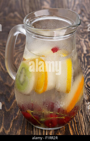 Glass pitcher of homemade detox water enriched with cherries and frozen fruit wedges. Misted jug full of cold water with popsicl Stock Photo