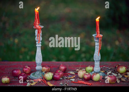 Twin candles burn on a table of apples at dusk. Stock Photo