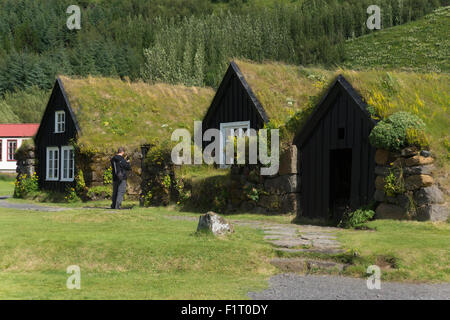 A male tourist sightseeing and using a camera phone to take a picture at the traditional turf houses at Skógarsafn - Skogar Museum in Iceland Stock Photo