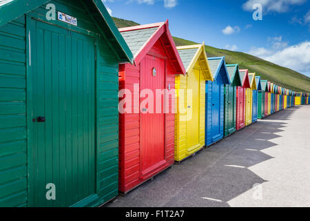 Row of colourful beach huts and their shadows with green hill backdrop, West Cliff Beach, Whitby, North Yorkshire, England, UK Stock Photo