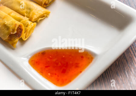 Four freshly cooked Thai style spring rolls on  a white plate with a red sweet chili dipping sauce with nobody present Stock Photo