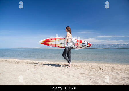 Woman carrying surfboard on beach Stock Photo