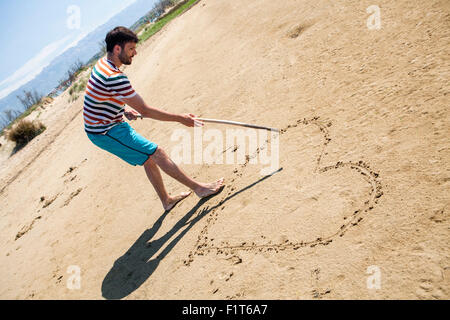 Man on beach drawing heart in sand Stock Photo