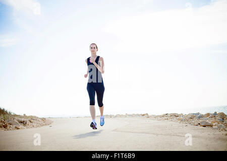 Young woman running on waterfront path Stock Photo