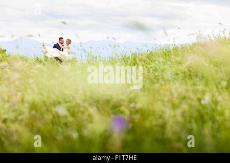 Groom carrying bride on meadow Stock Photo