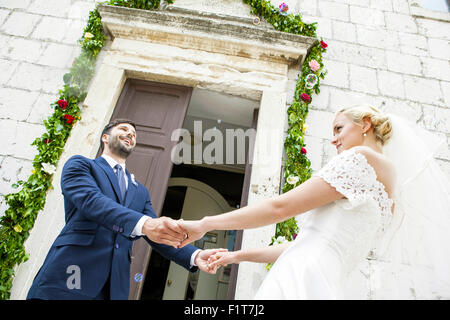 Bride and groom holding hands in front of chapel Stock Photo