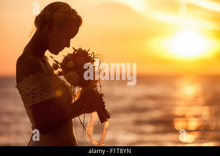 Bride smelling bouquet against sunset Stock Photo