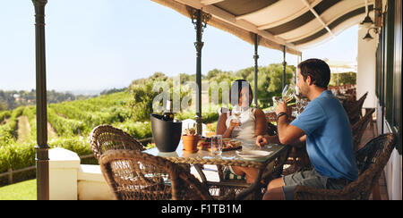 Couple enjoying a glass of wine in a vineyard. Young man and woman drinking white wine while sitting at a table on a wine cellar Stock Photo